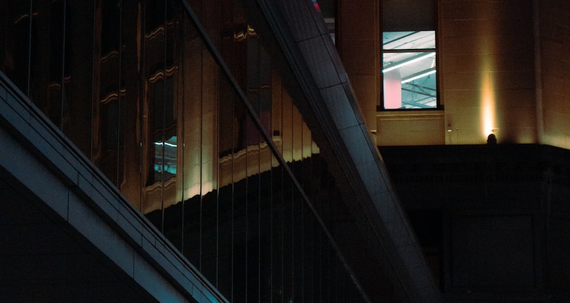 A night scene featuring a building with illuminated neon signage displaying 'CASINO'. The environment is urban with reflections on glass windows and glowing street traffic lights below. The atmosphere is dimly lit, with artificial lighting casting vibrant colors.